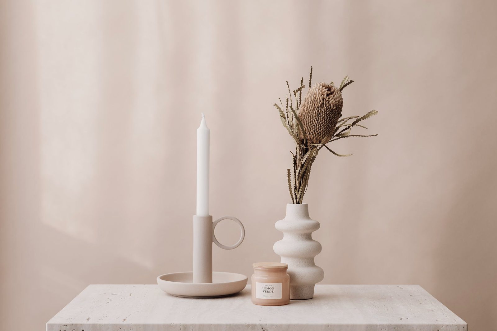 A candle, a small vase and dried flowers arranged on a pale surface