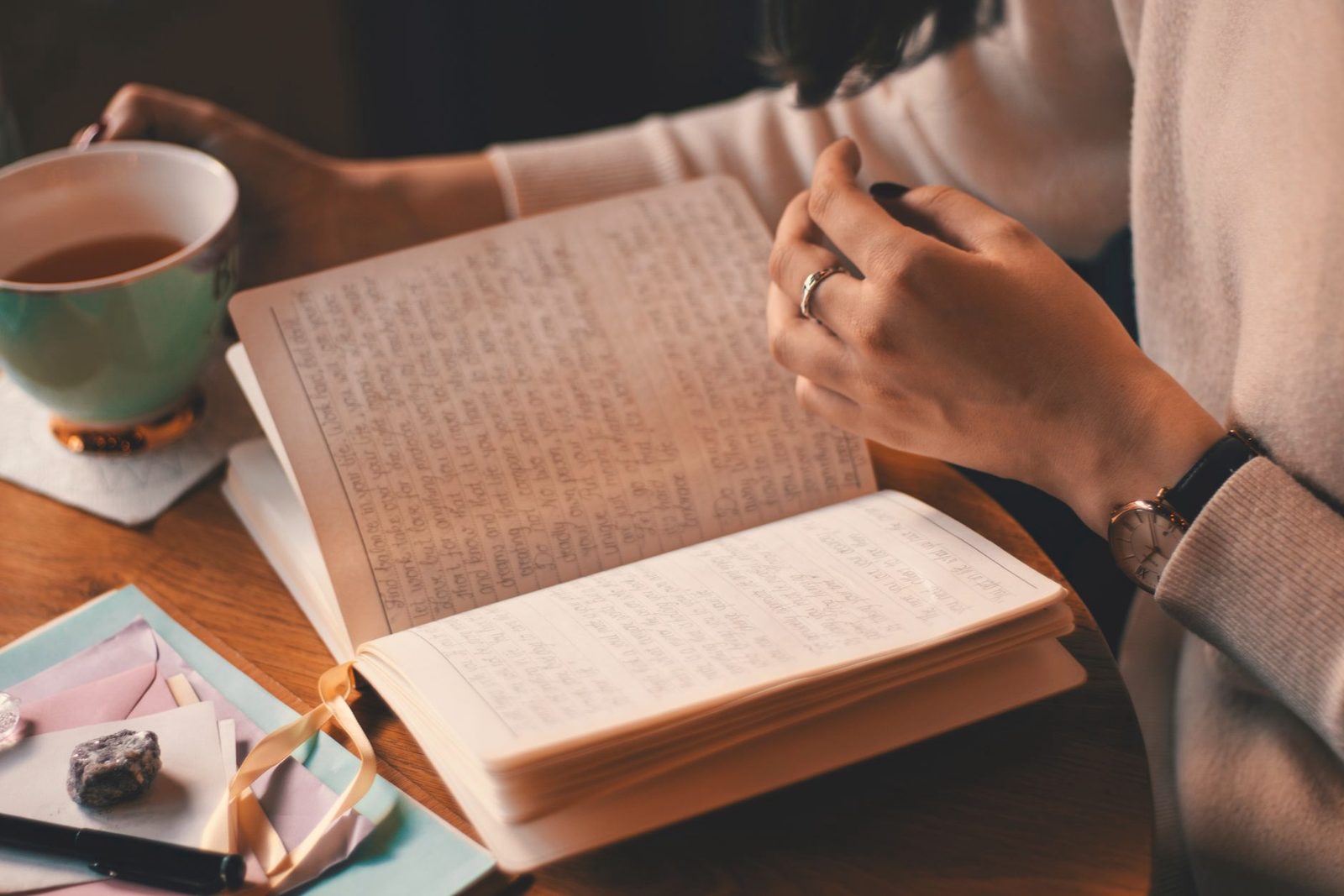 A woman’s hands resting on an open journal beside a cup of tea in warm light