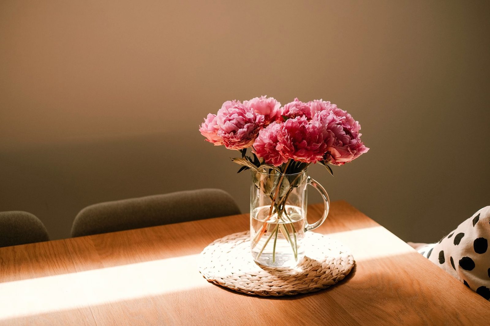 Pink peonies in a glass vase on a sunlit table
